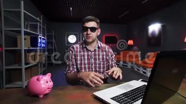 热情的戴墨镜的人在镜头前讲话，桌子上有猪和笔记本电脑
